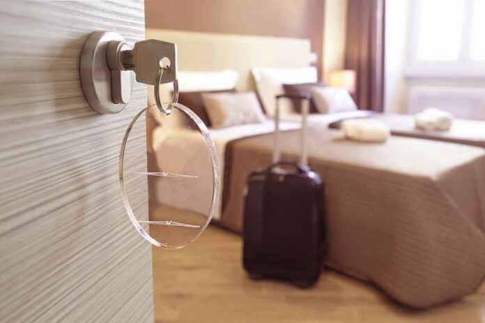 Hotel room key in door with suitcase by bed