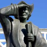 Bronze statue of a historical figure saluting against a blue sky