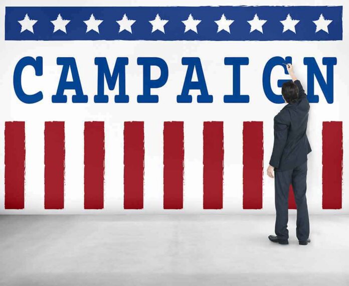 shutterstock_486646441-1 Man in suit writing on large campaign banner with stars and stripes