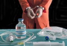 Handcuffed person in orange jumpsuit behind medical vials and IV equipment